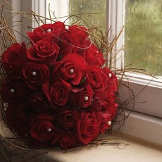 Red rose bouquet with twigs on windowsill next to rainy window