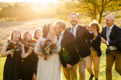 A bride and groom kiss while their wedding party cheers