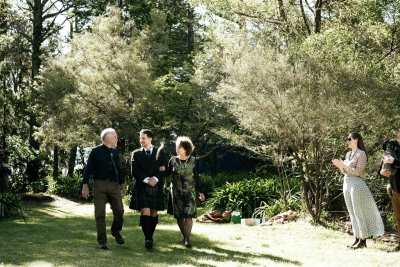 A groom wearing a kilt walks down the aisle in the arms of both his parents