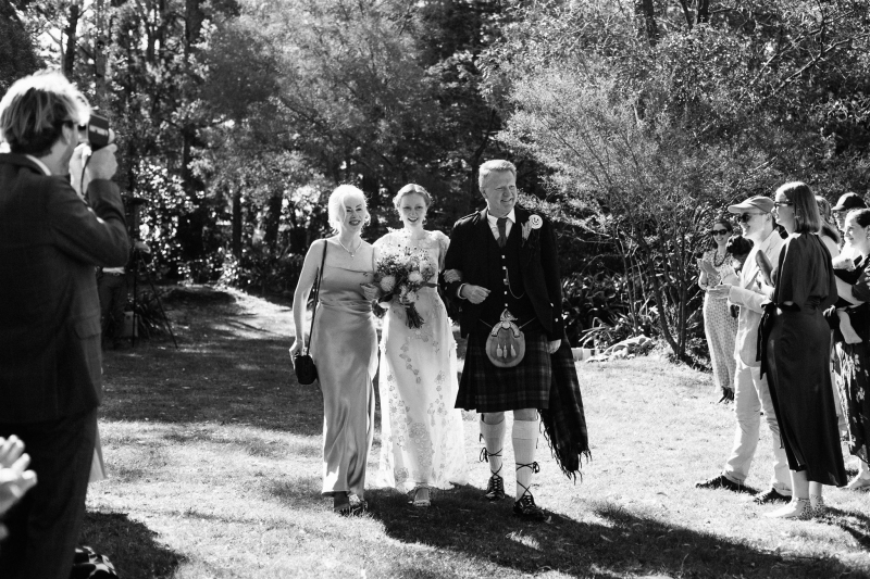 A bride wearing a vintage wedding dress walks down the aisle in the arms of both her parents