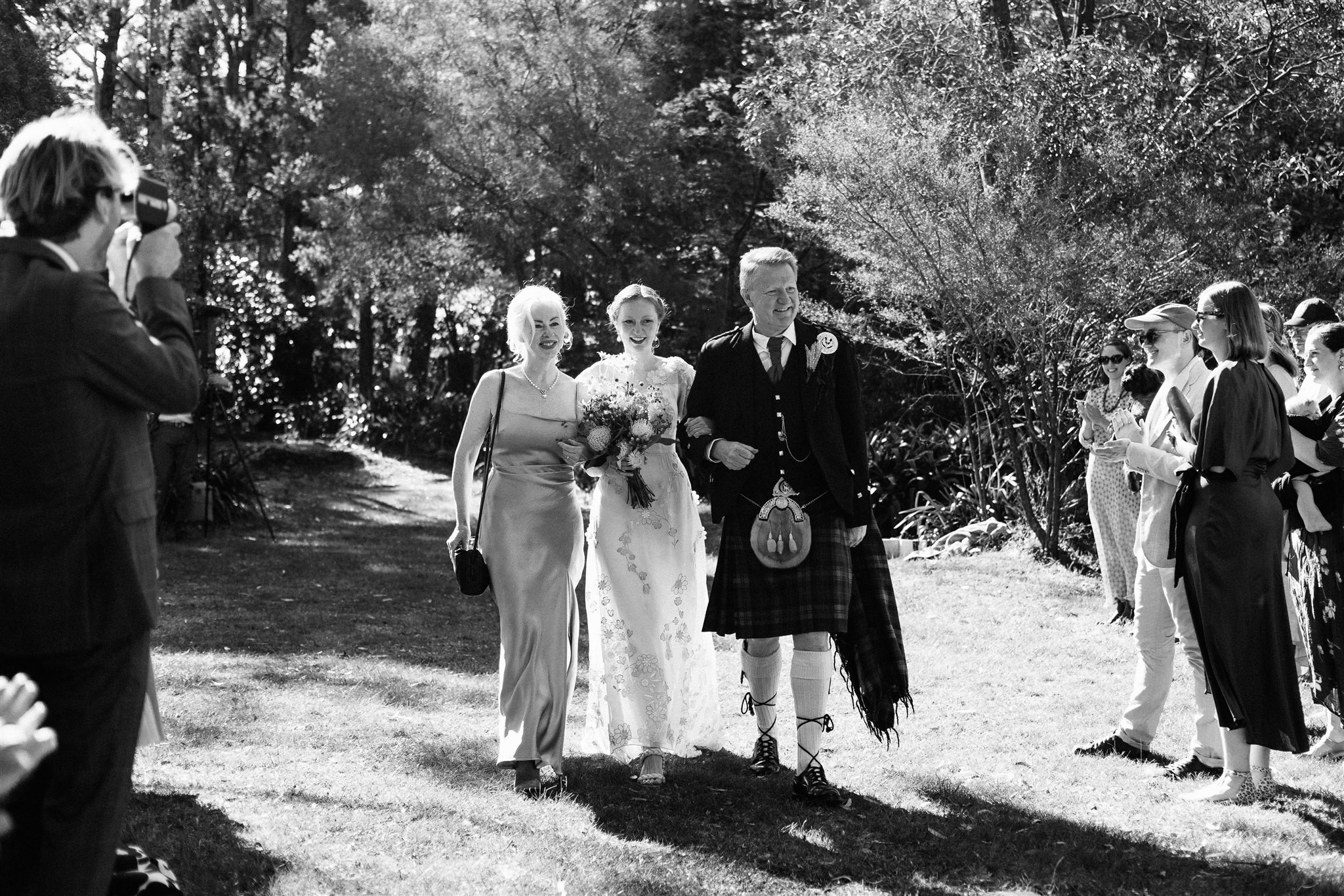A bride wearing a vintage wedding dress walks down the aisle in the arms of both her parents