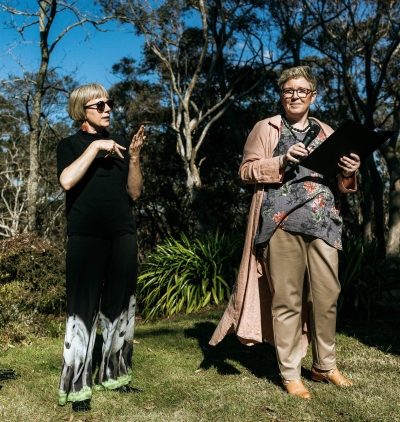 A groom wearing a kilt and a bride wearing a vintage wedding dress both read their vows to each other in their wedding ceremony in the Blue Mountains, with an Auslan interpreter