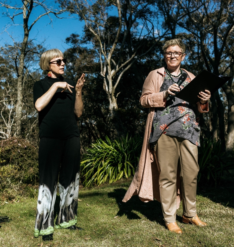 A groom wearing a kilt and a bride wearing a vintage wedding dress both read their vows to each other in their wedding ceremony in the Blue Mountains, with an Auslan interpreter
