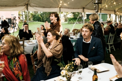 A crowd of wedding guests gather under a tent and clap for the bride and groom
