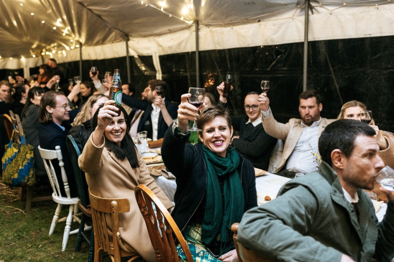 A crowd of wedding guests gather under a tent and toast the bride and groom