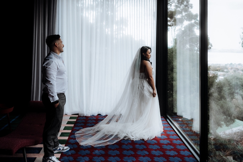 A bride and groom are dressed glamorously and are looking out the window of their Airbnb in Hobart Tasmania