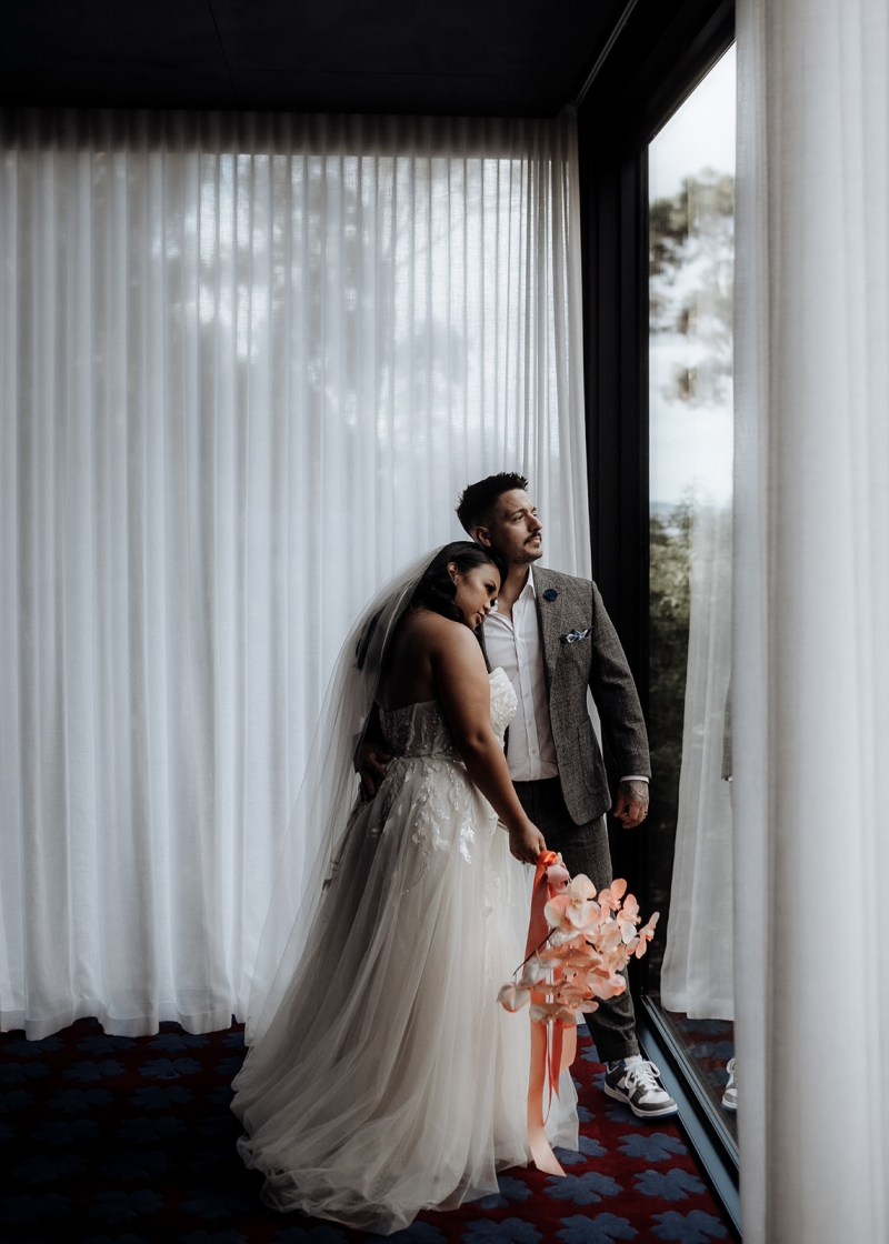 A bride and groom embrace and look out the large windows of their beautiful Airbnb in Hobart, Tasmania