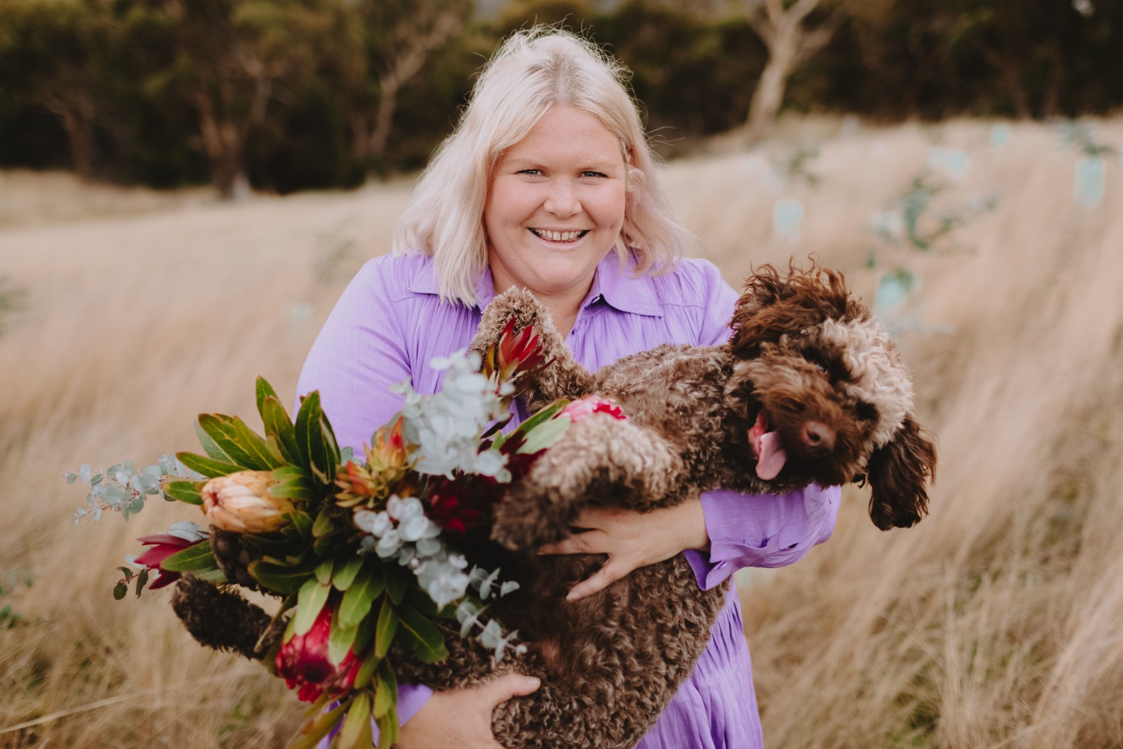 Nikki Davey from Grown Not Flown is standing in a field holding flowers and a chicken